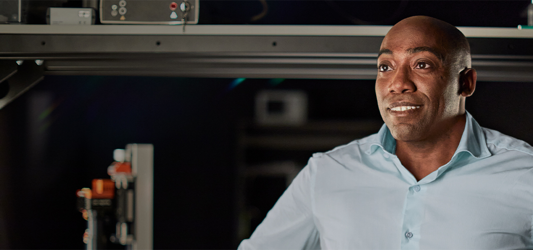 مايك يبتسم وينظر بعيداً إلى اليسار في منشأة هندسية، وهو محاط بالمعدات.