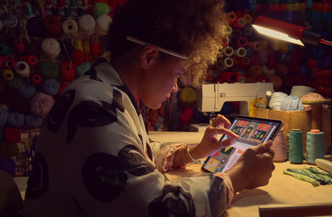 Une personne assise à un bureau utilise deux doigts sur l’écran d’un iPad pour agrandir une image.