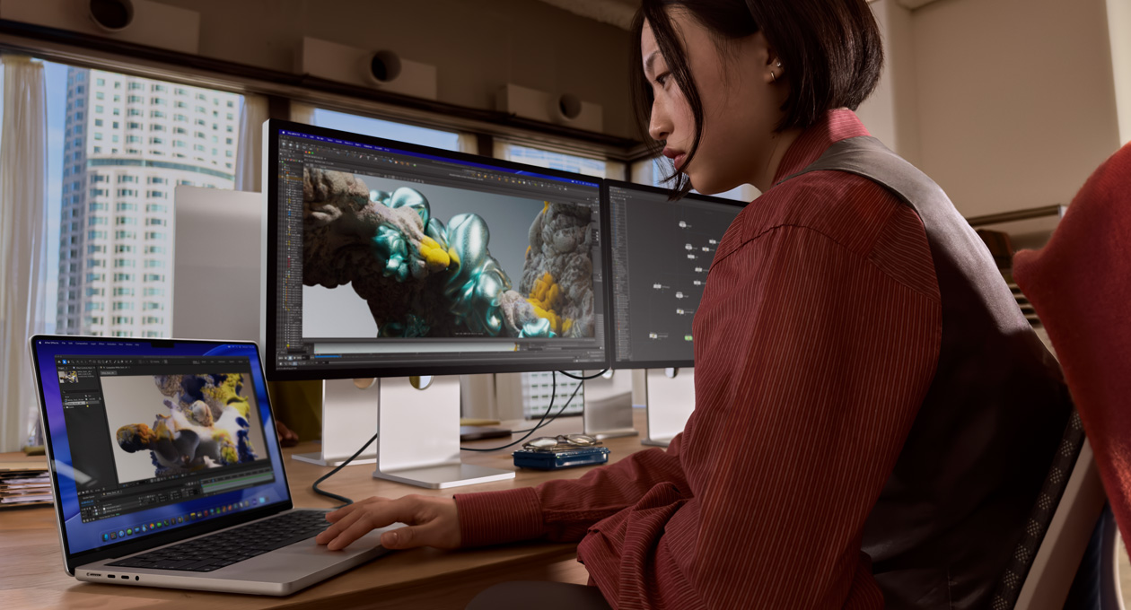 Seseorang di kantor bekerja menggunakan laptop MacBook yang terhubung ke Studio Display XDR melalui port Thunderbolt 5