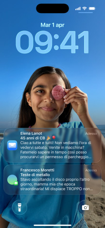 iPhone, cinque modelli, ogni modello si sovrappone leggermente a quello vicino, lo schermo all’estrema sinistra mostra una conversazione con uno sfondo in Messaggi, il secondo schermo da sinistra mostra la schermata Home con le icone delle app colorate, il modello al centro mostra la schermata di blocco con foto, i numeri dell’ora in Liquid Glass, due notifiche appaiono nella parte inferiore dello schermo, il secondo modello da destra mostra le icone delle app trasparenti in Liquid Glass, il modello all’estrema destra mostra il lettore musicale in Liquid Glass