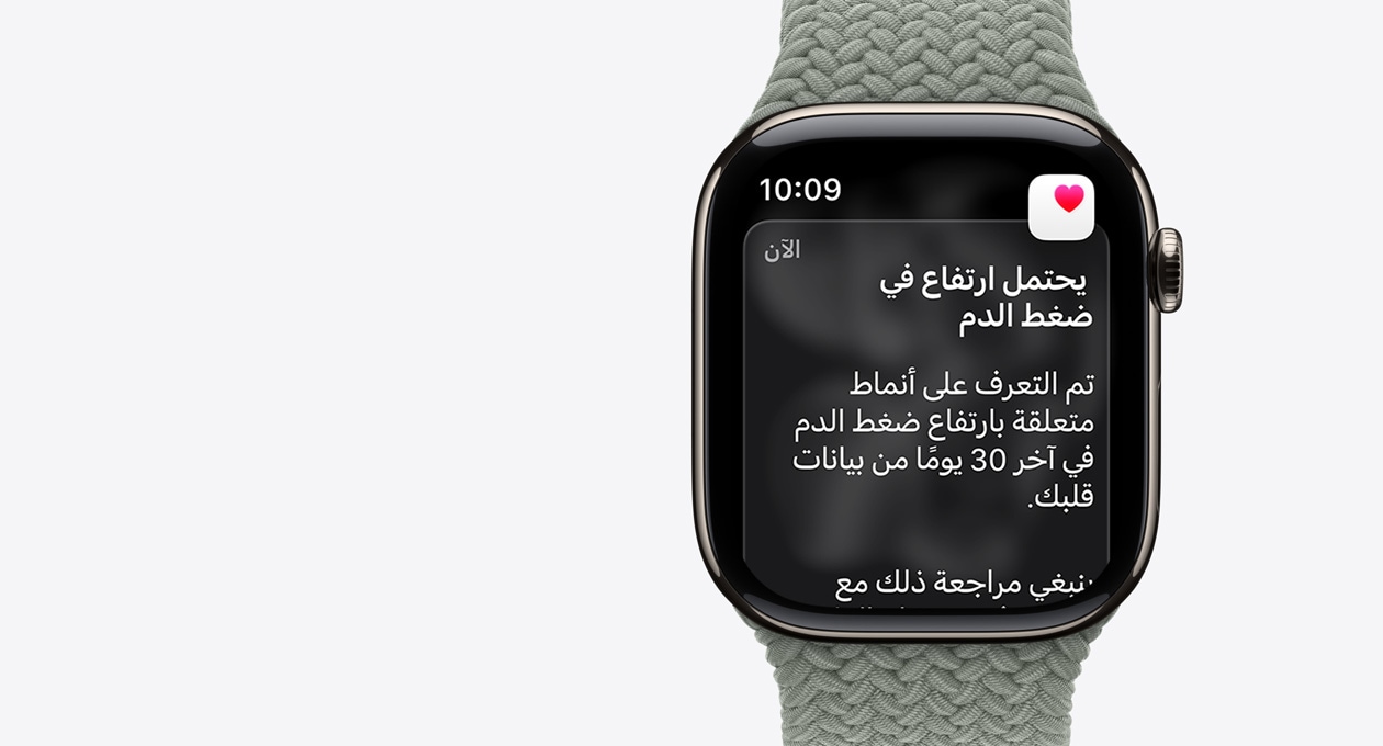 ساعة Apple Watch Series 11، لون طبيعي، إطار من التيتانيوم، إشعار بارتفاع محتمل في ضغط الدم، قلب وردي في خانة بيضاء، الجزء الخارجي الأيمن، التاج الرقمي، حزام، حزام Loop أحادي مَجدول بلون رمادي مخضر