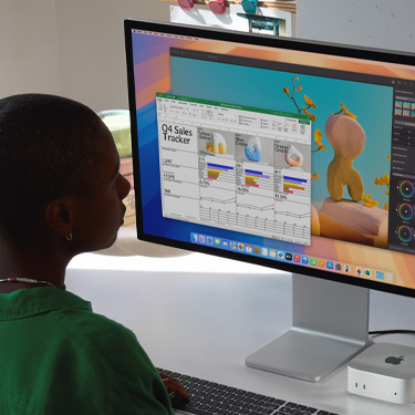 Woman working on an Excel spreadsheet on a Mac, sitting at a work table. The Excel spreadsheet is a Q4 sales tracker. Behind the Excel spreadsheet window is a Pixelmator Pro window.