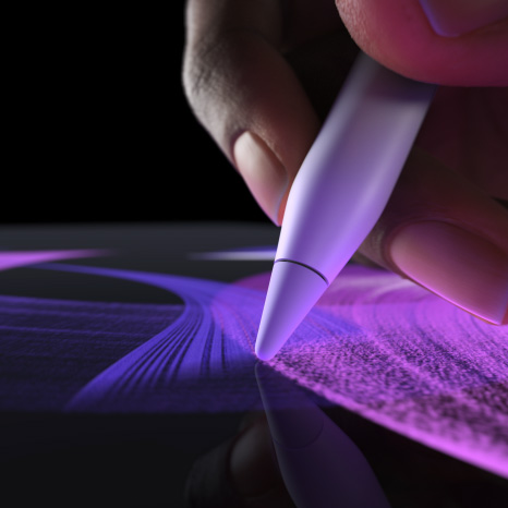 „Apple Pencil Pro“, iš šono, baltos spalvos, rankoje laikomas pieštukas ir piešiama ryškios mėlynos spalvos linija teptuku