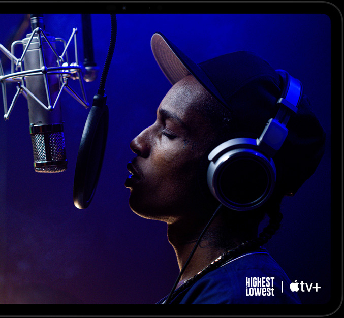 „iPad Pro“, horizontalioje padėtyje, priekinė pusė, kosminės juodos spalvos, užapvalinti kampai, juodas ekrano rėmelis, ekrane rodomas „AppleTV+“ vaizdas, kuriame matoma scena iš „Apple TV+“ originalaus filmo „Highest 2 Lowest“ su ASAP Rocky, vaidinančiu Yung Felon, kuris repuoja į mikrofoną