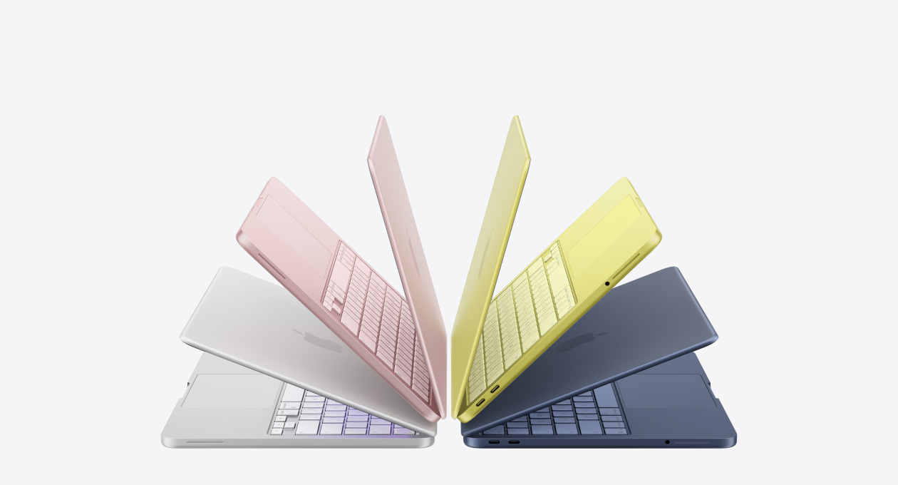 MacBook Neo laptops in silver, blush, citrus, and indigo colors, slightly open and arranged in an arch formation