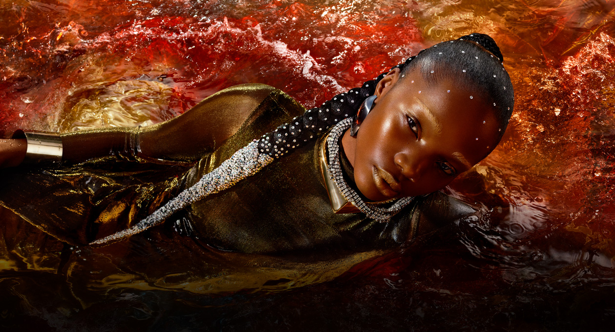 A model in a metallic gold dress lies on her side in a red pool of water, showcasing the brightness, contrast, and wide color gamut available on Studio Display XDR