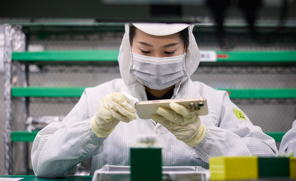 An employee in full-coverage work suit wipes an iPhone with a cloth at a work station