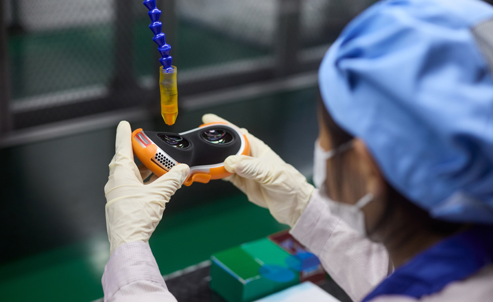 An employee wearing latex gloves holds parts of an Apple Vision Pro at an assembly facility